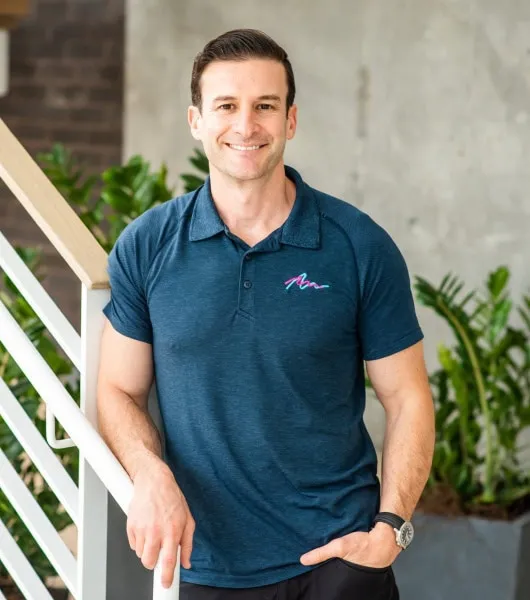 Dr. Jeff Goldberg, orthodontist at Davis & Goldberg Orthodontics, smiling in a polo shirt, standing beside a staircase with greenery in the background, emphasizing personalized orthodontic care.